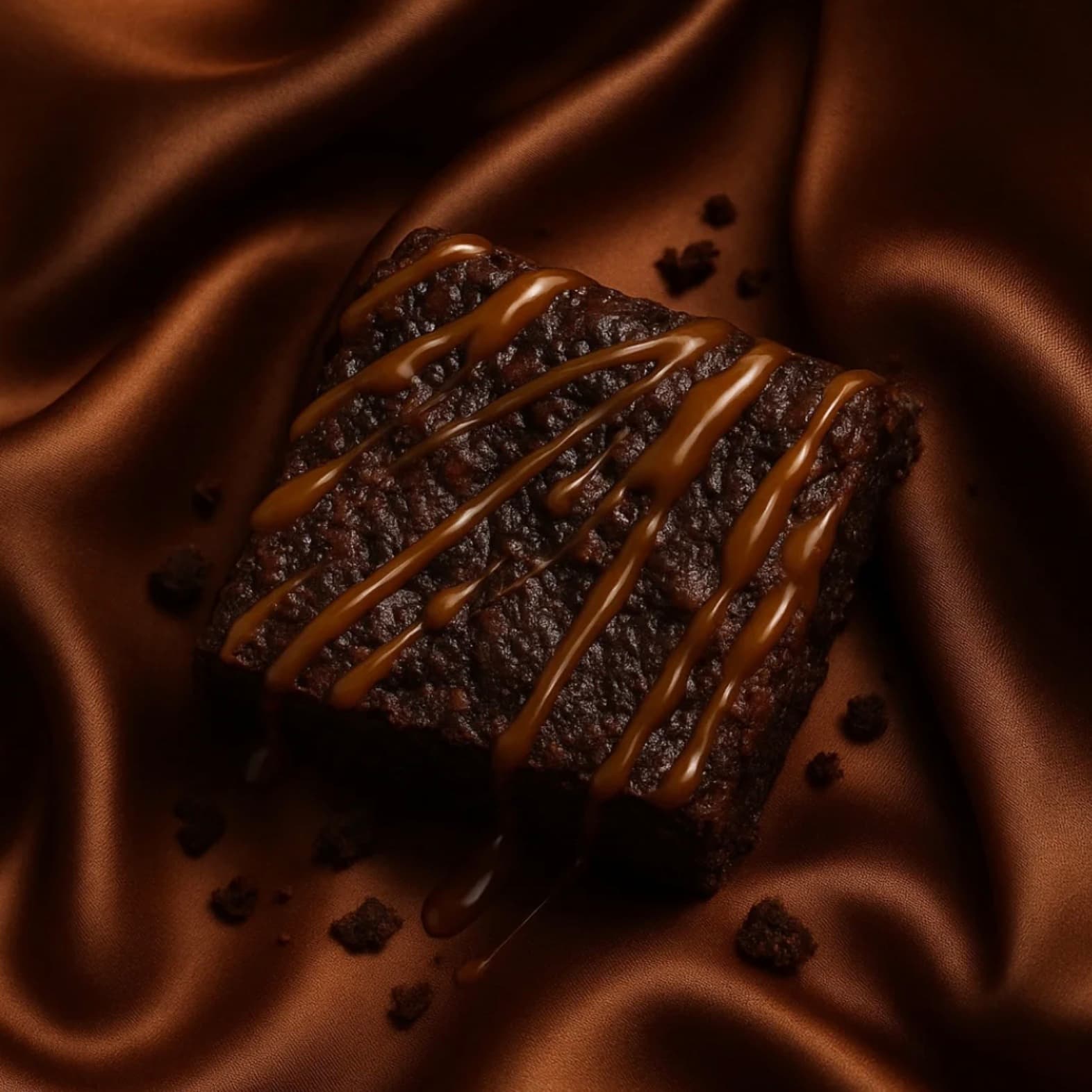 Caramel-drizzled brownie resting on rumpled copper satin